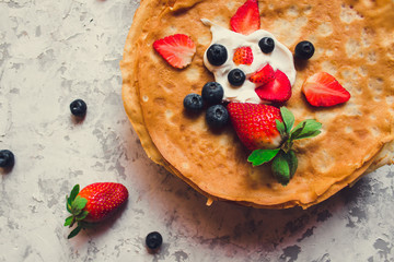 Overhead stack of thin pancakes poured with sour cream and decorated with fresh strawberries and blueberries. The concept of Russian holiday Maslenitsa, Shrovetide