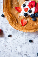 Overhead stack of thin pancakes poured with sour cream and decorated with fresh strawberries and blueberries. The concept of Russian holiday Maslenitsa, Shrovetide
