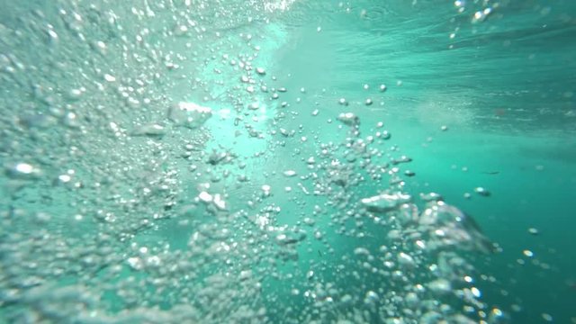 UNDERWATER SLOW MOTION: Mesmerizing underwater barrel wave creating numerous air bubbles raising to the surface. Rich blue colored ocean in the Canary Islands. Dynamic aquatic movement happening.