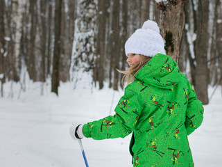 Little girl in a bright green suit trained skis in the woods.