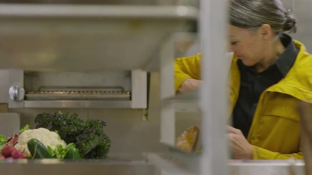 Handheld shot of female chef with crate of vegetables entering into commercial kitchen