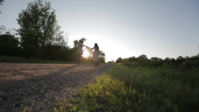 Man dancing with woman while holding guitar on dirt road against clear sky