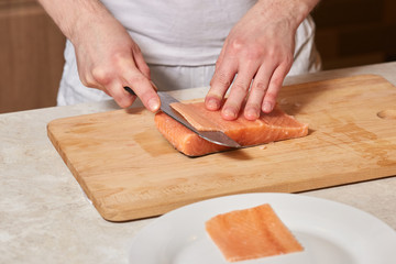 Chef making sushi rolls. Cutting salmon fish on wooden board