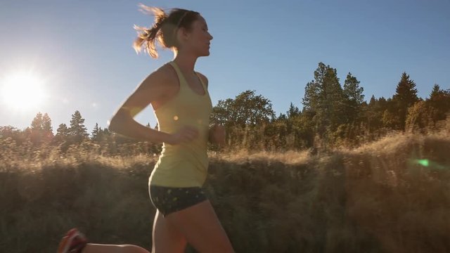 Steadicam shot of woman jogging by field on sunny day