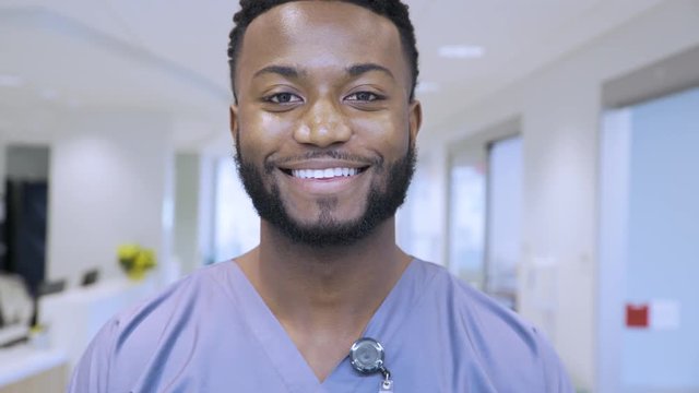 Handheld shot of young smiling male doctor standing at corridor in hospital
