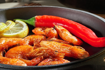 Fried shrimps with lemon and red pepper in cast-iron frying pan. Prepared at home restaurant dish. Wooden background.