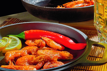 Fried shrimps with lemon and red pepper in cast-iron frying pan. Prepared at home restaurant dish. Wooden background.