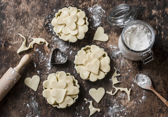 Flat lay Valentine's day baking background. Raw apple tartlets in the baking dish and baking ingredients on wooden background, top view