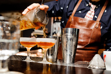 barman completes the preparation of two alcoholic cocktails using bar equipment