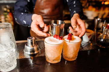 barman prepared two alcoholic cocktails Sour-mix of amber color with cherries and ice