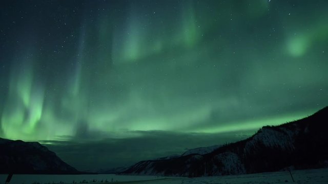 Time lapse shot of aurora borealis over lake and mountains against star field at Northern Rocky Mountains Provincial Park
