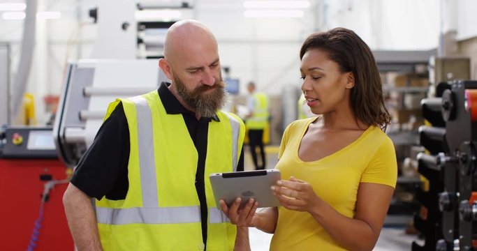 4k, Businesswoman and manager standing inside a printing and packaging plant with a digital touchscreen tablet. Slow motion.