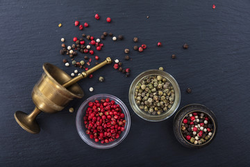 Peppercorns and a bronze mortar and pestle on black background, top view