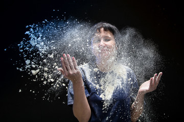 Woman with dark hair in a dark room and flying white powder