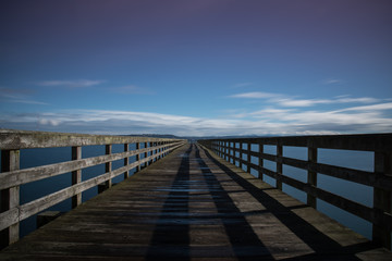 Fototapeta na wymiar Long boardwalk pier over water on a calm blue sky day