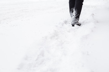 Man in black clothes going on white, fresh snow covered sidewalk after snowfall in winter day. City people in blizzard concept. Pavement is not cleaned from snow yet.