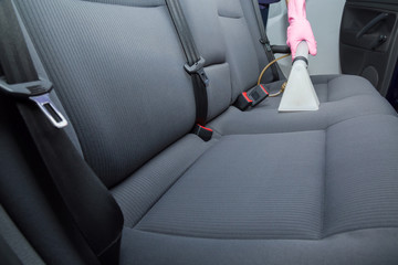 Dry cleaner's employee hand cleaning a car's gray textile seats with professionally extraction...