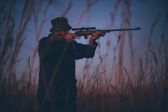 Hunter aiming prey on field with his rifle