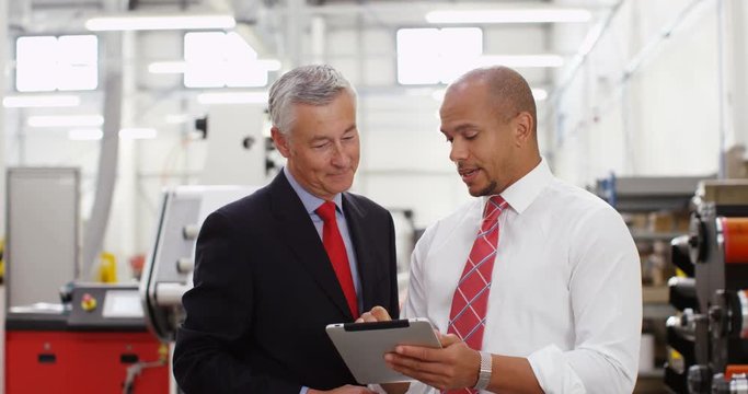 4K Business partners in factory looking at computer tablet & discussing operations. Crane shot panning downwards offering interesting change of background. Slow motion.