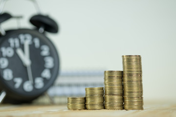 Steps of coins stack with vintage alarm clock and pen, notebook paper on wooden working table with copy space for text, financial and business planning concept..
