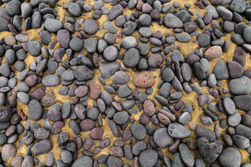 Round stones of volcanic origin, pebbles, on the beach sand, rounded and polished by sea water