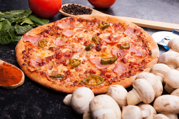 Fresh hot pizza next to the ingredients which it is made from on dark wooden background