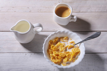 Corn Flakes cereal in a bowl, glass with milk and cap with espresso coffee. Morning breakfast.