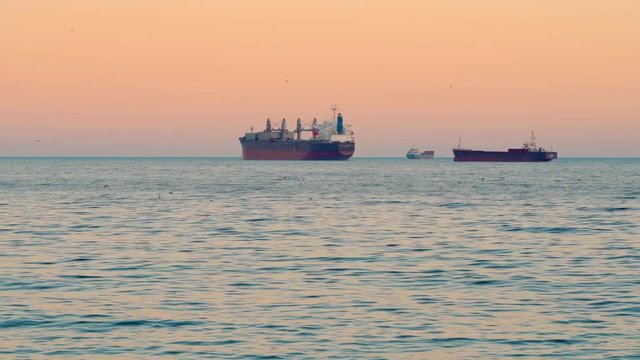 A bright dawn on the blue sea. Sea coast. Small waves on the water surface. Large commercial cargo ships on the horizon