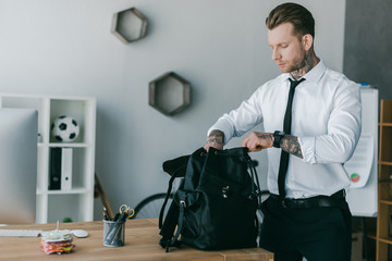 handsome young tattooed businessman opening backpack at workplace