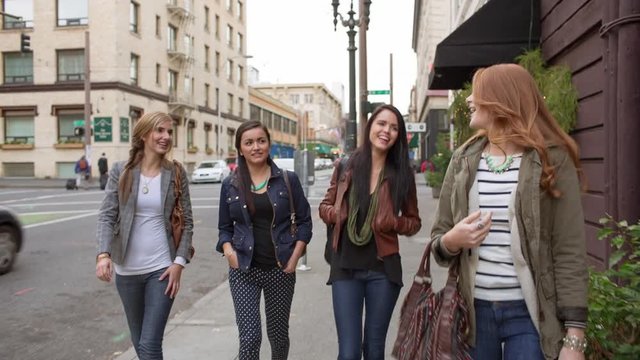 Handheld shot of female friends talking while walking at sidewalk in city