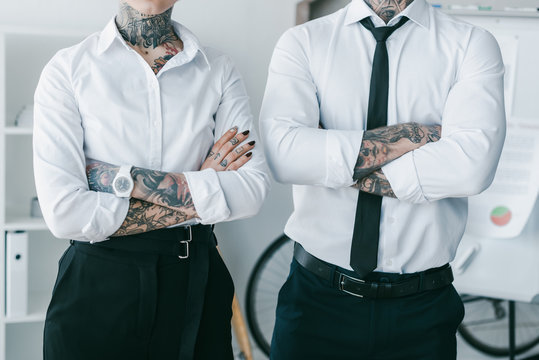 Cropped Shot Of Young Business People With Tattoos Standing With Crossed Arms In Office