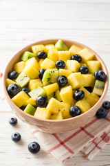 Fresh fruit salad with pineapple, mango, kiwi and blueberries on white wooden background.