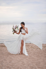 Fototapeta na wymiar bride in a boho style on the beach near the sea with a wedding bouquet