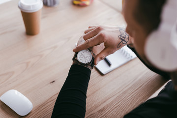 selective focus of young businessman checking wristwatch at workplace