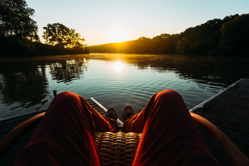 Young Man Sits In Armchair By The Lake And Meets Sunrise Or Sunset, Point Of View. Recration...