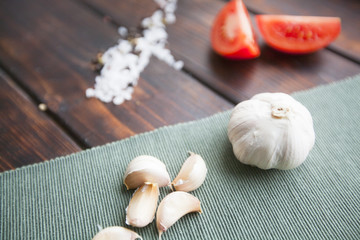 Diet, Italian Food Cooking, Vegetarian Concept. Sliced tomato, sea salt grains and black pepper corns scattered on a dark wooden table and a bulb of garlic on a linen napkin