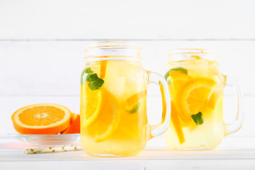 Orange detox water in mason jars on a white wooden table. Healthy food, drinks.