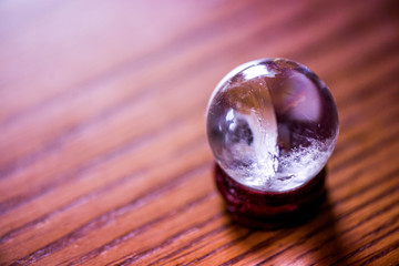 Fortune telling. A macro shot of a glass ball on a wooden pad, with sun reflections, bubbles and a rainbow in it, standing on a pine dining table in the middle of a kitchen