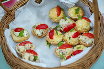 Cheese snacks with tomato slices and herbs in wooden basket. Leftovers from birthday celebration