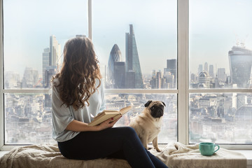 London view from window. Woman with dog sitting next to the window with book and enjoying amazing...