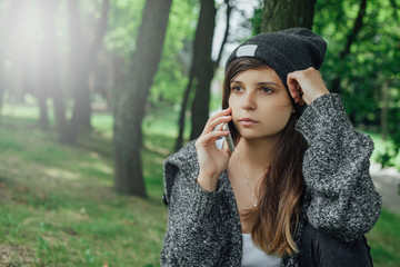 Młoda kobieta rozmawia przez telefon w parku. - obrazy, fototapety, plakaty