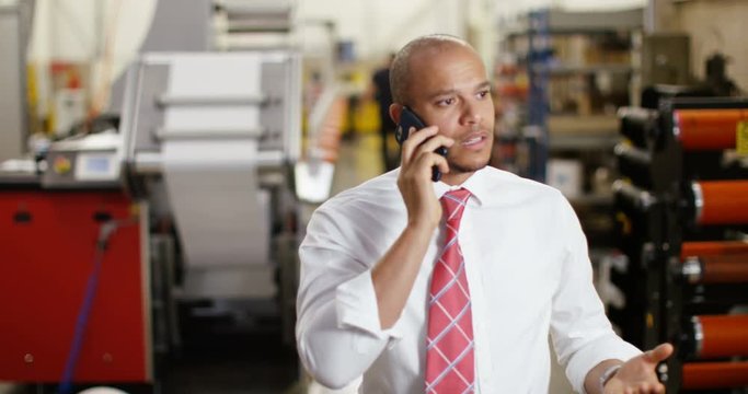 4K Frustrated & annoyed businessman in factory dealing with business problems over the phone. Slow motion.