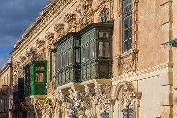 Fototapeta premium Traditional Maltese blue wooden balconies, typical yellow beige sandstone or limestone architecture in Valletta, capital city of Malta, known as Il-Belt.