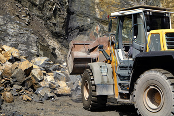 a wheel loader / front loader machine working on a heap of stones with its shovel at a quarry