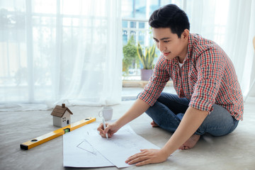 Young handsome male asian architect working at home on the floor.