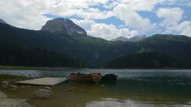 Panoramic image of a mountain lake in Montenegro. Summer period on the Black Lake below the Durmitor Mountain. On a wooden dock, moored boats.