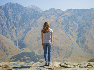 Fototapeta premium Hiker with backpack standing on top of the mountain and enjoying valley view at sunrise