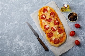 Oval Italian pizza with tomato Margarita on gray concrete background. Selective focus. Top view....