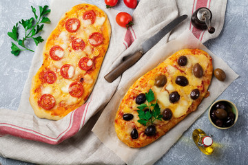 Two different oval Greek pizza with olives and tomato Margarita on gray concrete background....