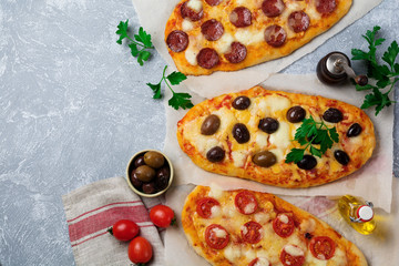 Three different oval pizza with olives, tomato and salami on a gray concrete background. Selective...